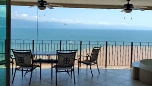 A balcony with a table and chairs overlooking a beach and ocean.
