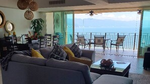 A living room with a grey sofa, a coffee table, and a view of the sea through a glass door.