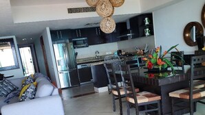 A modern kitchen with dark cabinets, a dining area with a round table and chairs, and a living room with a sofa and a coffee table.