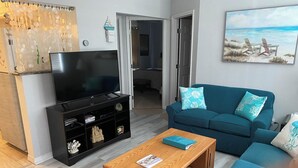Un soggiorno con televisore, tavolino in legno e divano verde acqua con cuscini decorati.