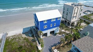 A two-story building with a blue facade and a white roof, adjacent to a beach with waves. - Sweeping Views, Oceanfront Porches, Private Beach Access, Close to Lighthouse - Double Stack (Folly Beach)