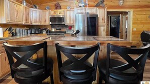 Ein Interieur einer Holzhütte mit einer Küche, die Holzschränke, einen Edelstahlkühlschrank und eine Pendelleuchte zeigt.