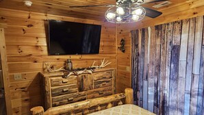 Ein rustikaler Holzraum mit einem Bett, einem an der Wand befestigten Fernseher und einem Deckenventilator.