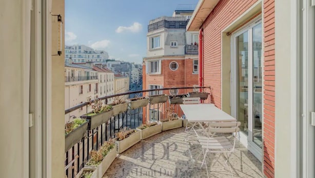 Un balcón con mesa y sillas, un edificio rojo y vistas a otros edificios.