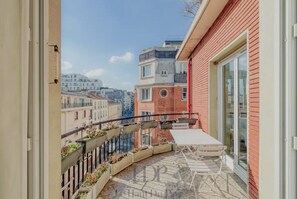 En balkon med et bord og stole, en rød bygning og udsigt til andre bygninger.
