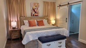 A bedroom with a wooden bed, beige curtains, a painting on the wall, a bedside lamp, and a sliding door to the bathroom. - New Home 3/2 With Garage Near Downtown (Mount Dora)