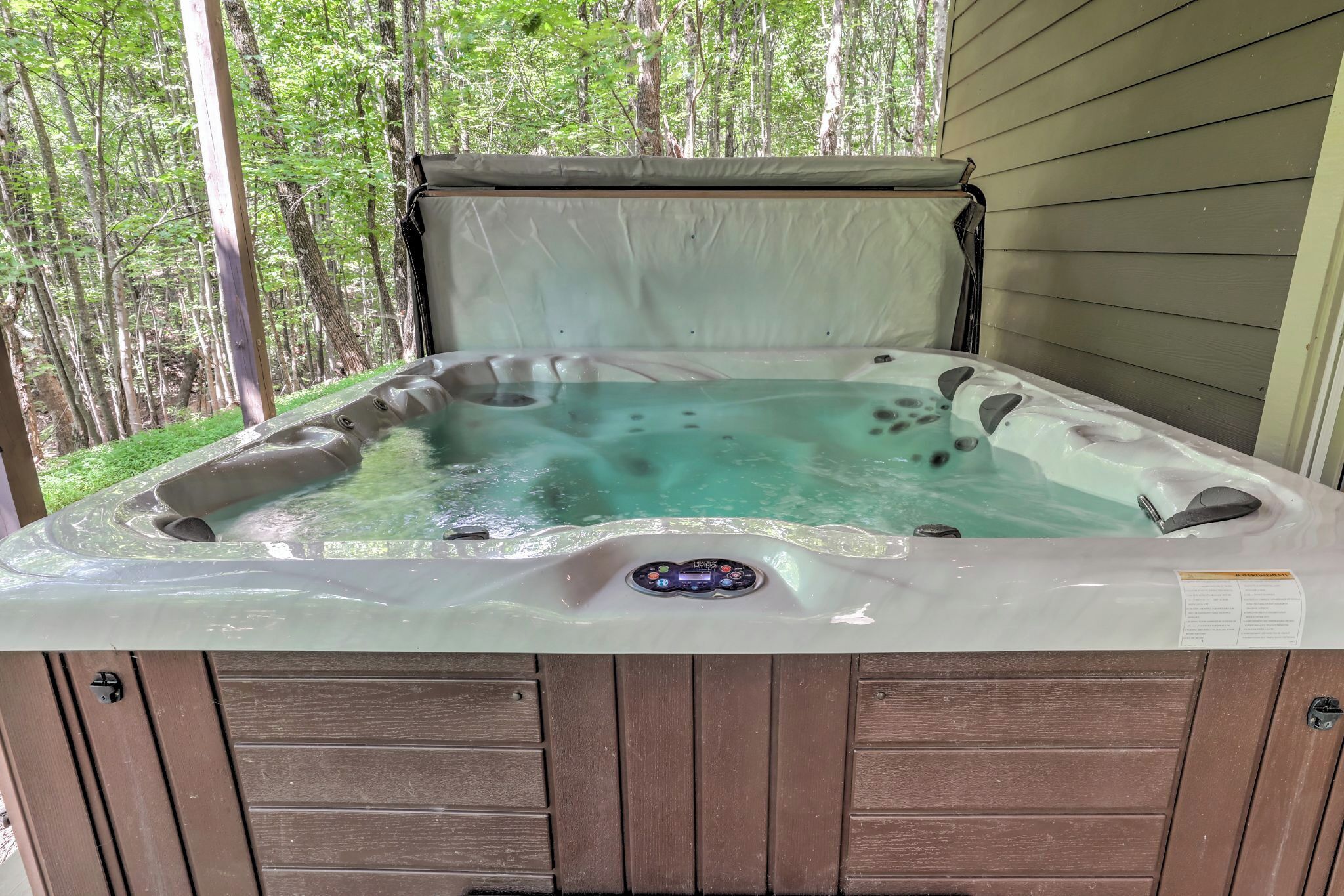 Un jacuzzi con panel de control, rodeado de paneles de madera y un paisaje boscoso.