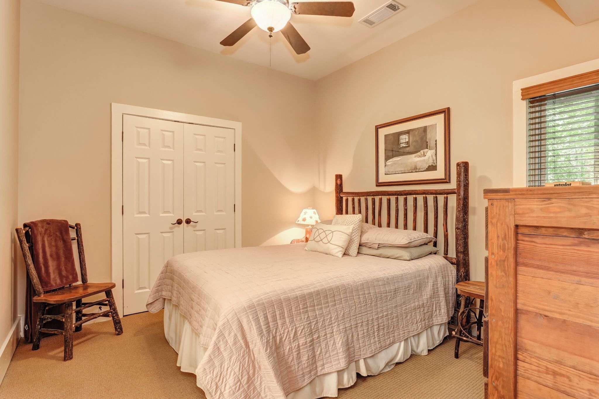 A bedroom with a bed, a wooden chair, a wooden dresser, a ceiling fan, and a framed picture on the wall.