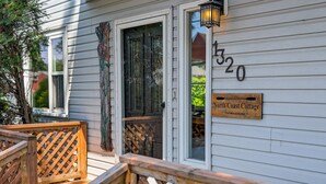 A wooden deck with a lattice railing, a wooden sign indicating 'North Coast Cottage' at 1320 Minnesota Ave, and a window with a decorative door. - Beach Retreat on Park Point | Hot Tub • Fire Pit • Beach Access (Duluth)