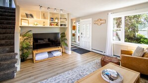 A living room with a TV, wooden flooring, a sofa, a coffee table, and a staircase. - Beach Retreat on Park Point | Hot Tub • Fire Pit • Beach Access (Duluth)