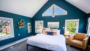 A bedroom with a large bed, a chair, a nightstand, and a window with a view of greenery. - Beach Retreat on Park Point | Hot Tub • Fire Pit • Beach Access (Duluth)