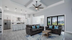 A spacious living area with a modern kitchen, two sofas, a coffee table, and a large window offering a view of the outdoors. - Pool overlooking canal, Outdoor Grilling station - Villa Sand Dollar Siesta (Cape Coral)