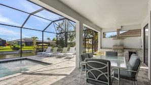 A modern outdoor patio with a pool, seating area, and a barbecue grill. - Pool overlooking canal, Outdoor Grilling station - Villa Sand Dollar Siesta (Cape Coral)