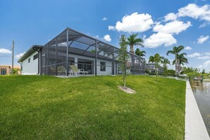 Une maison moderne dotée d’une grande extension en verre, d’une pelouse verdoyante et de palmiers.