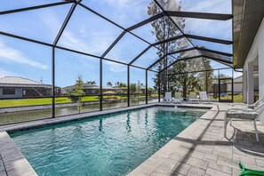 Une piscine entourée d’une structure en verre, donnant sur une terrasse aménagée avec des chaises longues et offrant une vue sur le quartier.