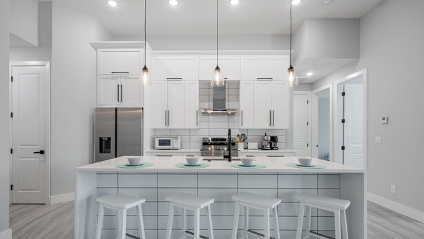 A modern kitchen with white cabinetry, a central island with stools, stainless steel appliances, and pendant lighting. - Pool overlooking canal, Outdoor Grilling station - Villa Sand Dollar Siesta (Cape Coral)