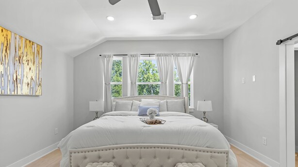 Une chambre spacieuse avec un grand lit, deux tables de chevet, une fenêtre avec des rideaux et un luminaire au plafond.