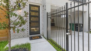 Une maison moderne avec une porte d’entrée noire, un portail en métal et un petit arbre dans le jardin.