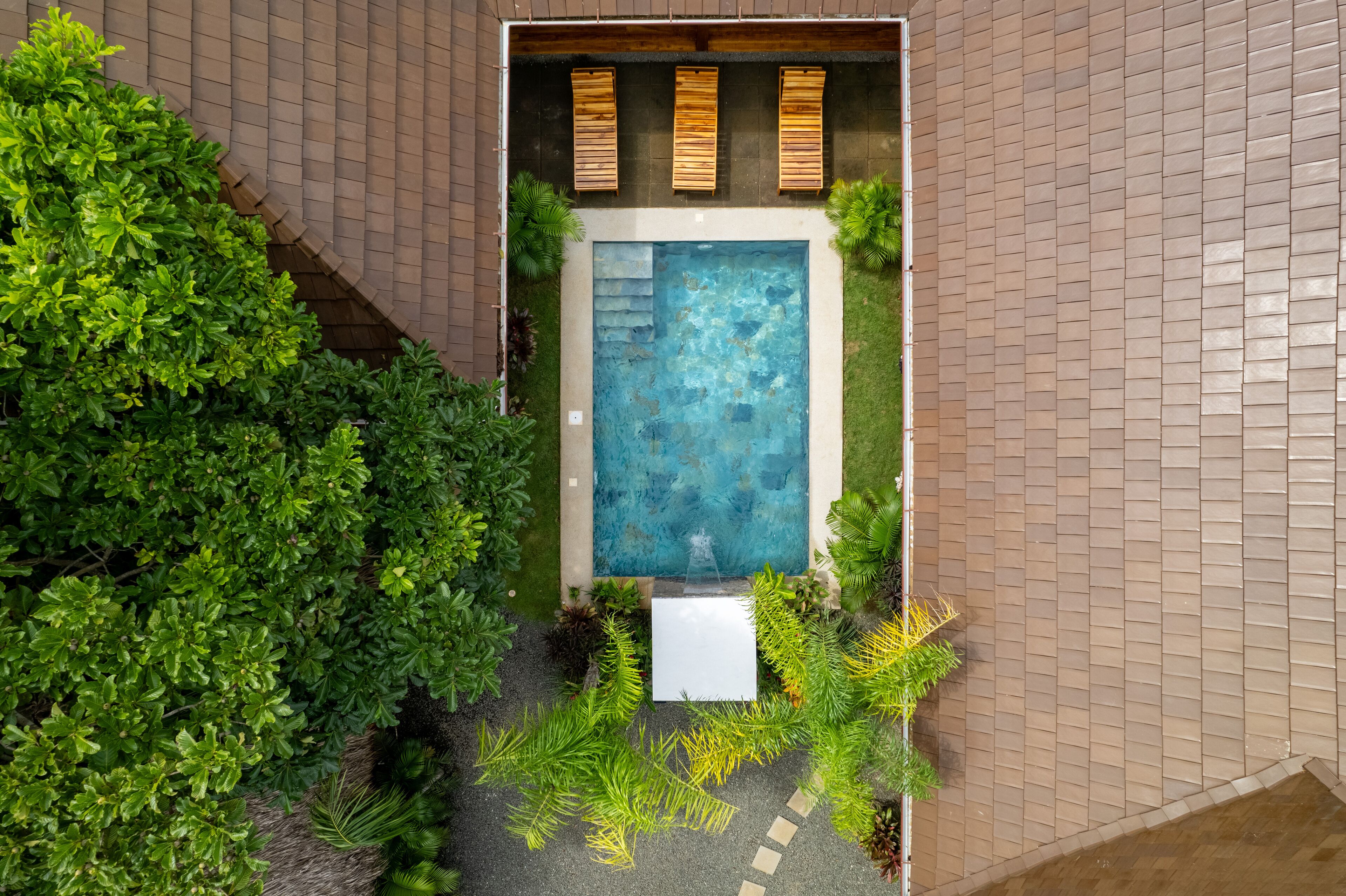 Vista aérea de un edificio moderno con piscina, rodeado de exuberante vegetación y fachada de ladrillo.