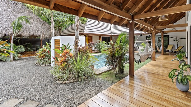 A covered outdoor area with a pool, wooden deck, and tropical plants. - Villa Ave del Paraíso (Veintisiete de Abril)