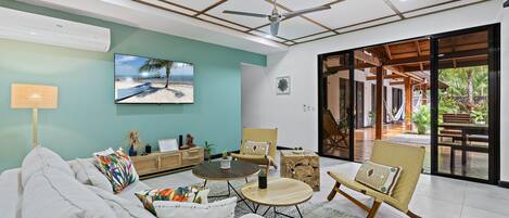 Un salon moderne comprenant un canapé, une table basse et des fauteuils, un téléviseur et une grande fenêtre donnant sur l’extérieur.