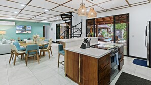 A modern kitchen with a central island, a dining area with chairs, and a staircase leading to a balcony. - Villa Ave del Paraíso (Veintisiete de Abril)