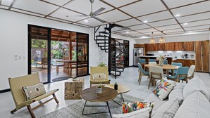 A spacious living area with a sofa, coffee table, and chairs, a dining area with a table and chairs, and a kitchen with wooden cabinets. - Villa Ave del Paraíso (Veintisiete de Abril)