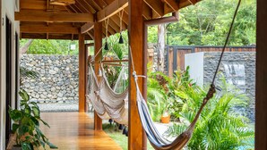 A wooden covered porch with a hammock, potted plants, and a stone wall. - Villa Ave del Paraíso (Veintisiete de Abril)