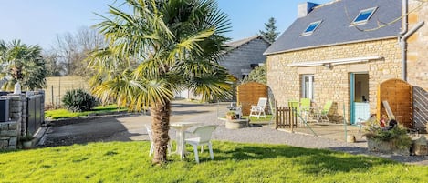Une maison en pierre avec une pelouse bien entretenue, un palmier et un espace salon extérieur.