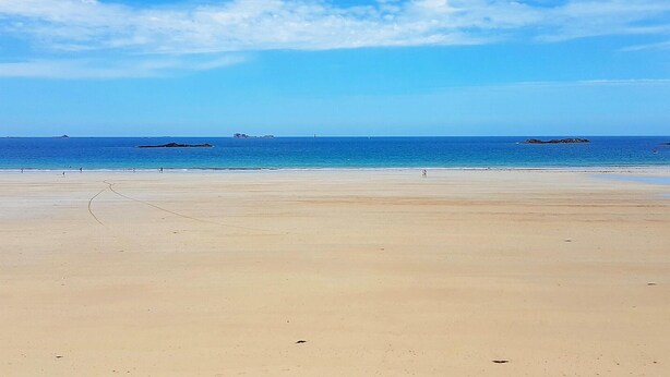 Una extensa playa de arena con cielo azul despejado y mar tranquilo.