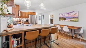 Uma cozinha moderna com armários de madeira, uma ilha central com banquetas, eletrodomésticos de aço inoxidável e iluminação pendente.