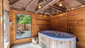 Uma cabana de madeira com hidromassagem, paredes rústicas e uma janela grande.