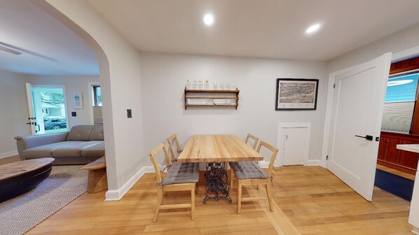 A dining area with a wooden table and chairs, a sofa, and a view of the outdoors.