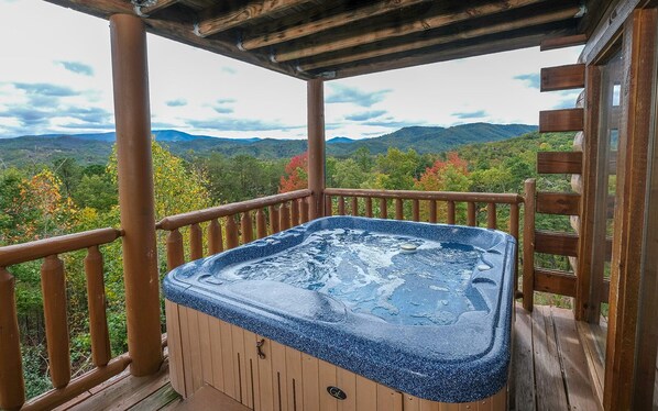 Un bain à remous sur une terrasse en bois, avec vue sur les montagnes et les couleurs automnales.