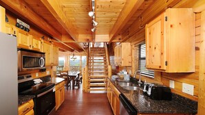 A wooden cabin-style kitchen with a central staircase, wooden cabinets, a microwave, and a sink. - Smoky Mountain Mist - Private Putt-Putt, Theater Room, + More! (Sevierville)