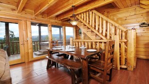 A wooden cabin interior with a dining area, wooden staircase, and large windows offering a view. - Smoky Mountain Mist - Private Putt-Putt, Theater Room, + More! (Sevierville)
