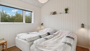 A bedroom with two beds, a window with a view of trees, a shelf with decorative items, and a pendant light. - 4 bedroom stunning home in Strandby (Strandby)