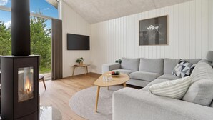 A modern living room with a fireplace, a sofa, a coffee table, and a TV mounted on the wall. - 4 bedroom stunning home in Strandby (Strandby)