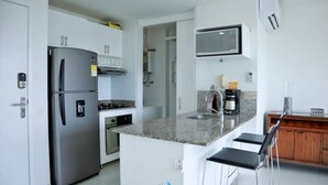 A modern kitchen with a built-in refrigerator, oven, and microwave. There is a granite countertop and a small island with bar stools. - Hermoso Apartamento Frente a la Playa (Cartagena de Indias)