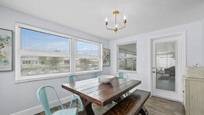 A dining area with a wooden table, light blue chairs, and a bench. There are large windows with blinds, a chandelier, and a door leading outside. - Waterfront Vacation Getaway (Hudson)