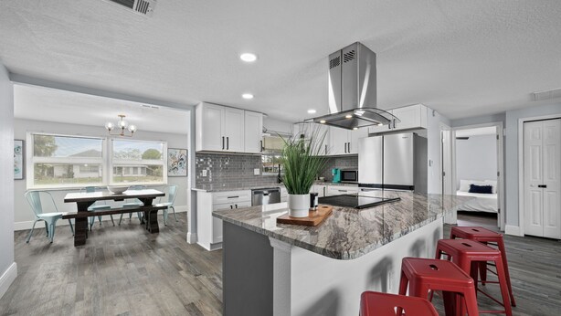 A modern kitchen with a large island, red bar stools, and a dining area with a table and chairs. - Waterfront Vacation Getaway (Hudson)