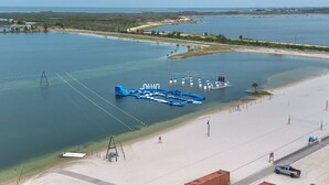 An aerial view of a coastal area with a sandy beach, a water body, and a blue floating structure with various amenities. - Waterfront Vacation Getaway (Hudson)