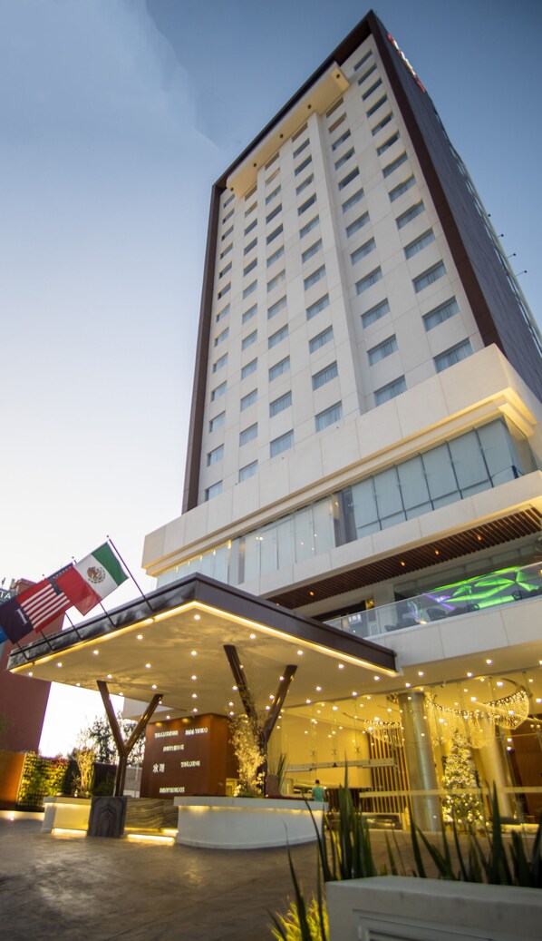 A high-rise hotel with a modern design, featuring a prominent entrance with a covered area and decorative lighting. - Sheraton Guadalajara Expo (Zapopan)