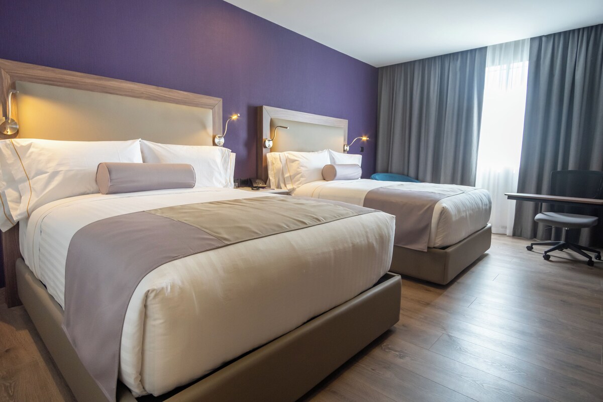 A hotel room with two beds, a desk, and a chair.