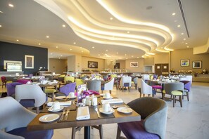 A spacious hotel dining area with multiple tables and chairs, a modern ceiling design, and a buffet setup. - Sheraton Guadalajara Expo (Zapopan)