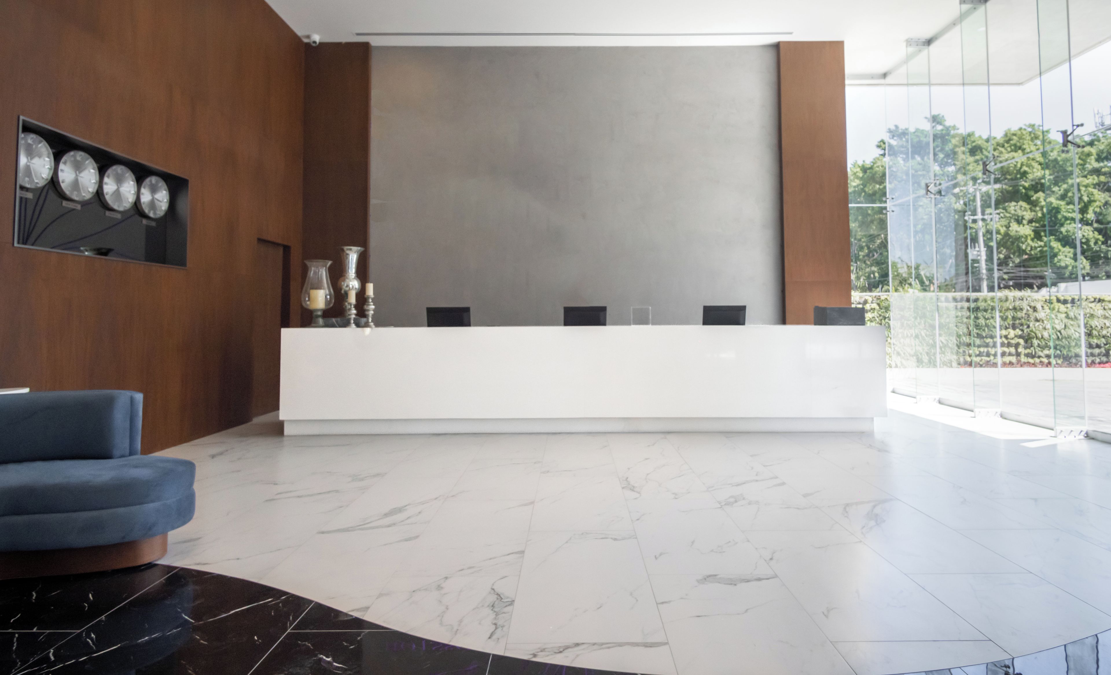 Un área de recepción moderna con suelo de mármol, un revestimiento de pared de madera y un ventanal con vistas a zonas verdes.