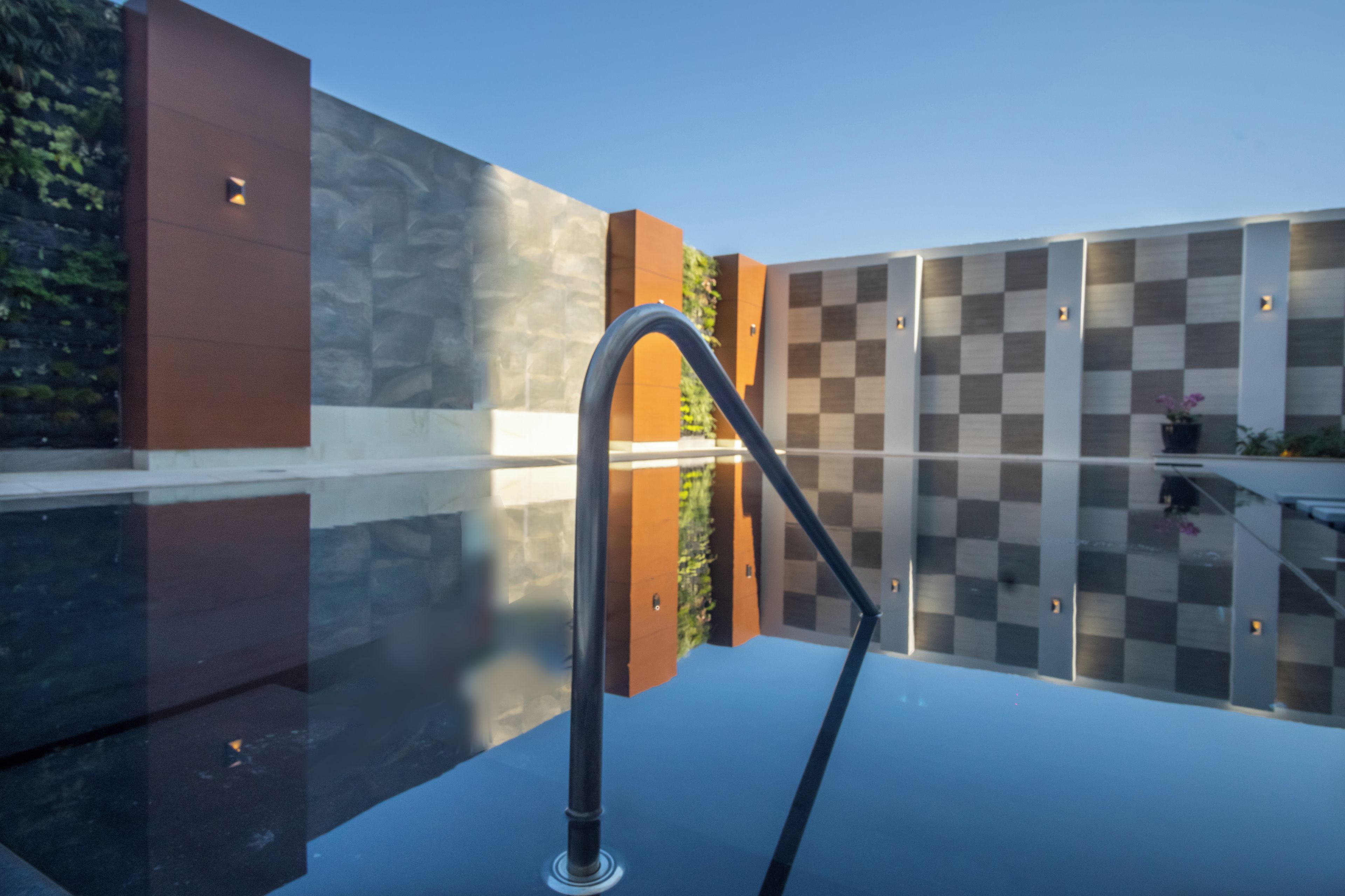 A modern outdoor pool area with a checkered wall, a metal railing, and a glass floor.