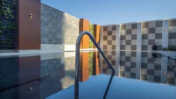 A modern outdoor pool area with a checkered wall, a metal railing, and a glass floor.