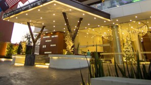 Un hôtel de grande hauteur au design moderne, doté d’une entrée imposante avec un espace abrité et un éclairage décoratif.