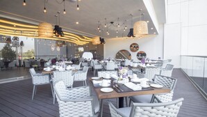 Un restaurant avec des chaises et des tables à coussins blancs, un éclairage suspendu et une vue sur l’extérieur.